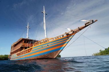 Large wooden sailing ship with blue and orange stripes anchored in clear ocean waters under a blue sky.